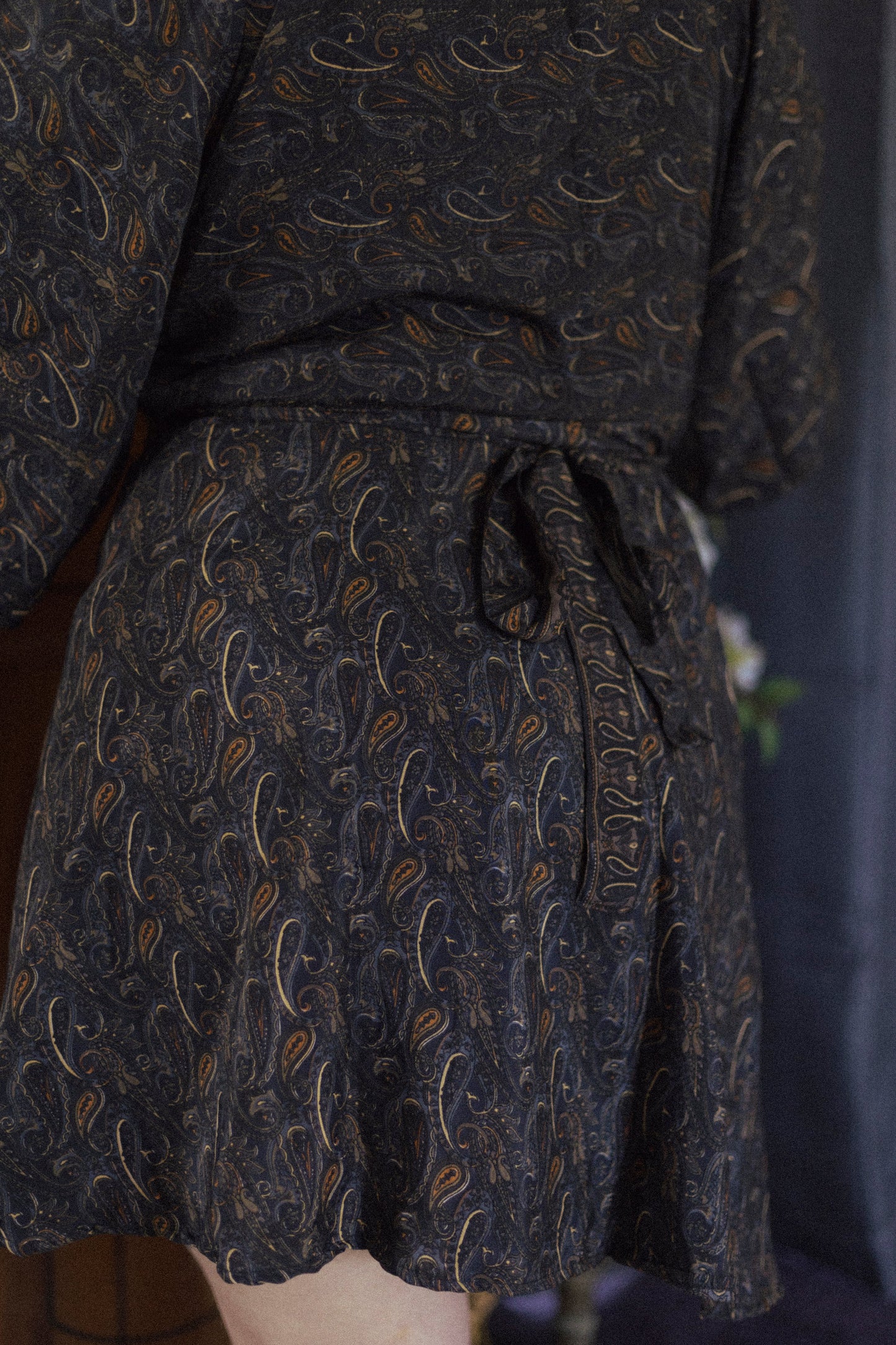 Dark patterned wrap dress tied at the waist on a plain background