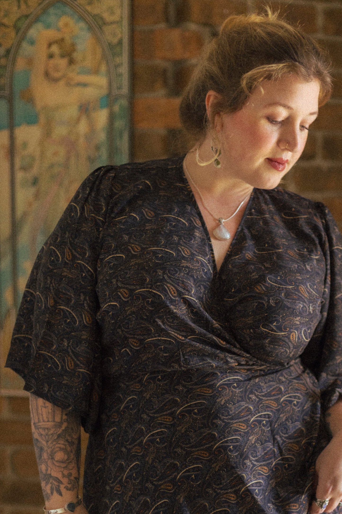 Woman wearing a dark patterned dress in front of a brick wall with decorative elements.