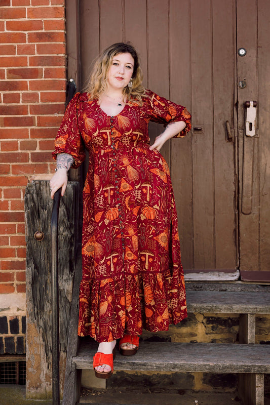 Woman in a red patterned dress standing on wooden steps against a brick wall.