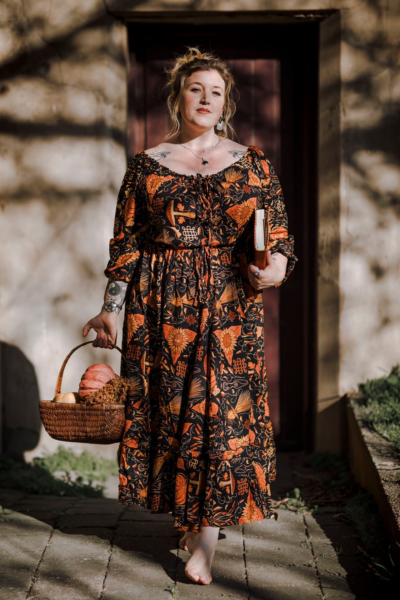 Woman in a mushroom patterned dress holding a basket of pumpkins outdoors