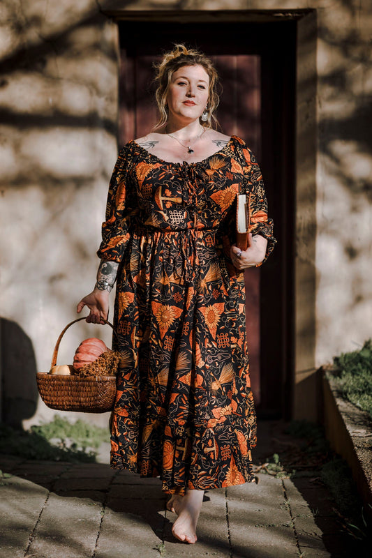 Woman in a mushroom patterned dress holding a basket of pumpkins outdoors
