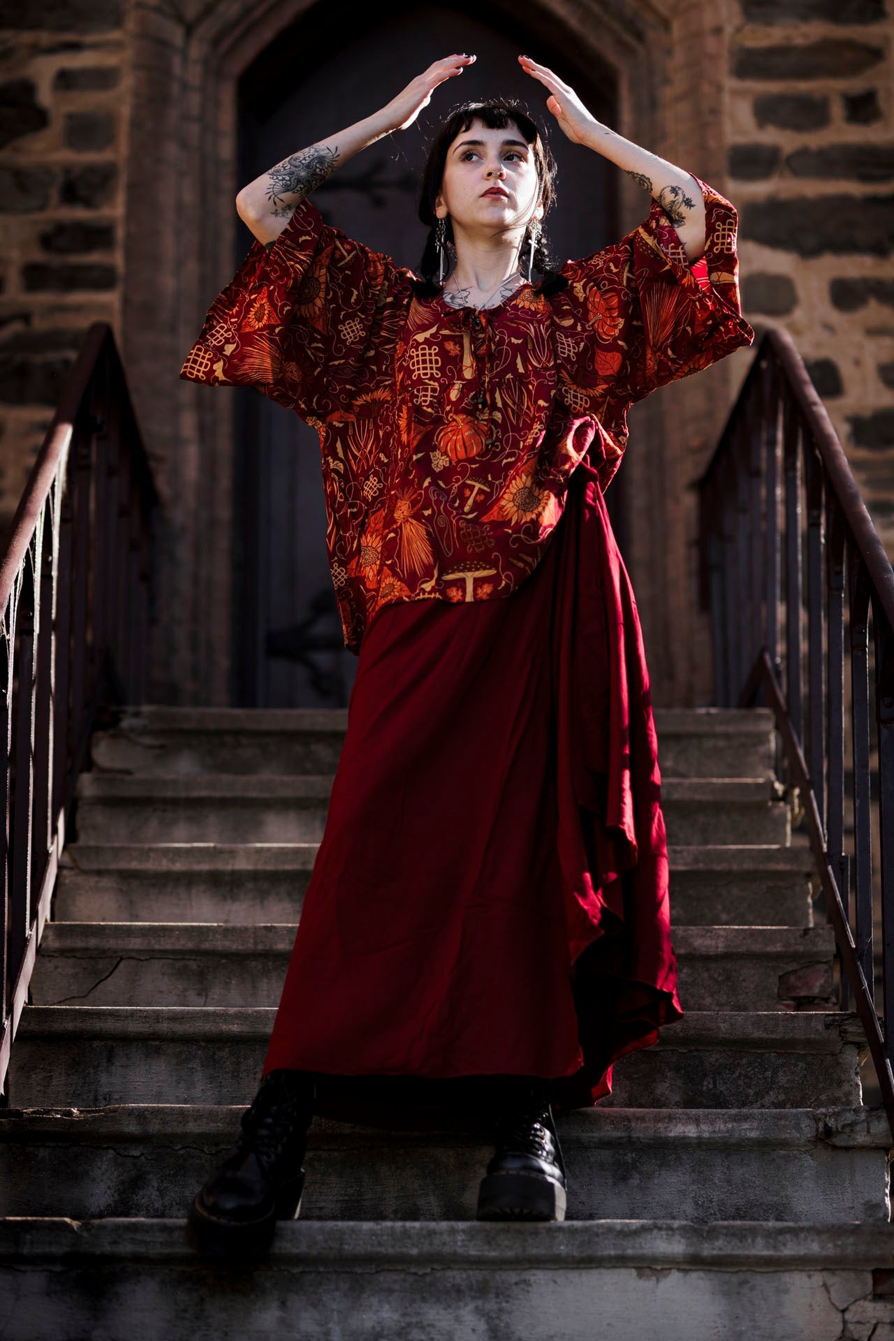 Person in a red and patterned top standing on stone steps with a stone building in the background
