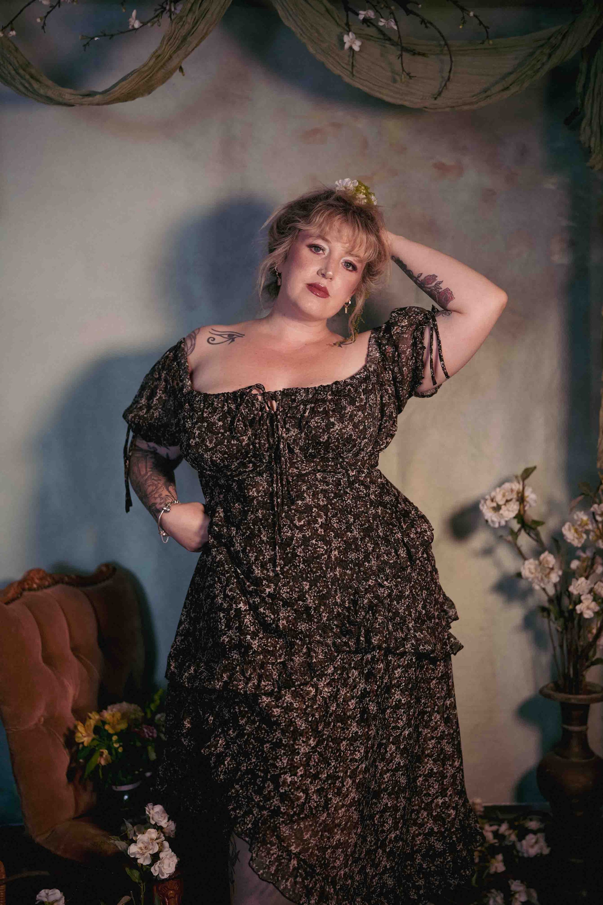 Woman in a floral dress standing against a decorative wall with flowers.
