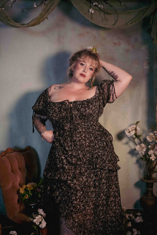 Woman in a floral dress standing against a decorative wall with flowers.